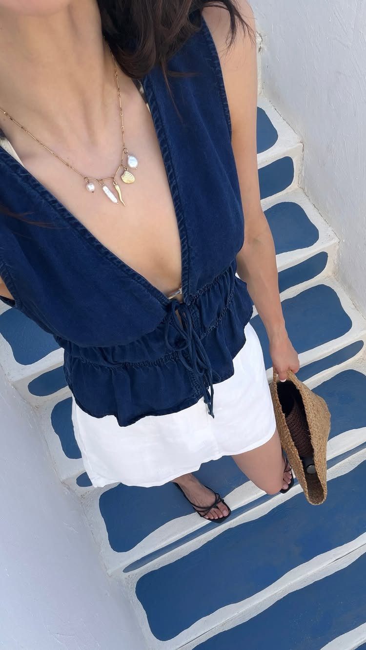 Woman in navy top and white shorts standing on blue and white stairs holding a straw hat.