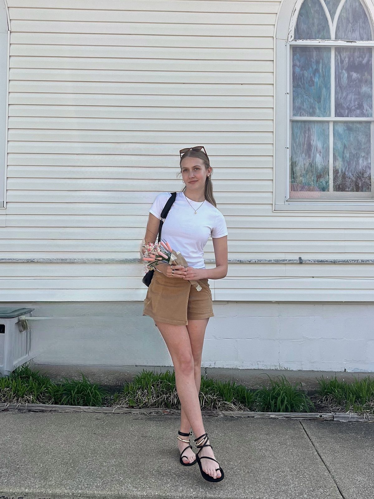 A woman in a white t-shirt and tan shorts standing outdoors in black sandals.