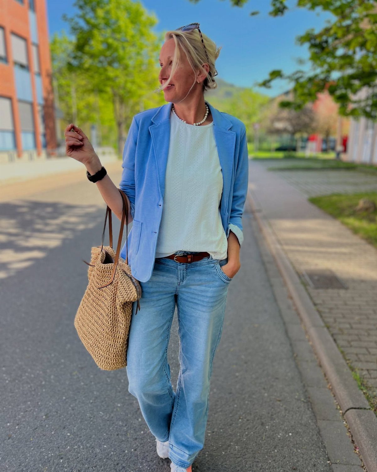 A woman walking in a blue blazer, white t-shirt, and light blue jeans.
