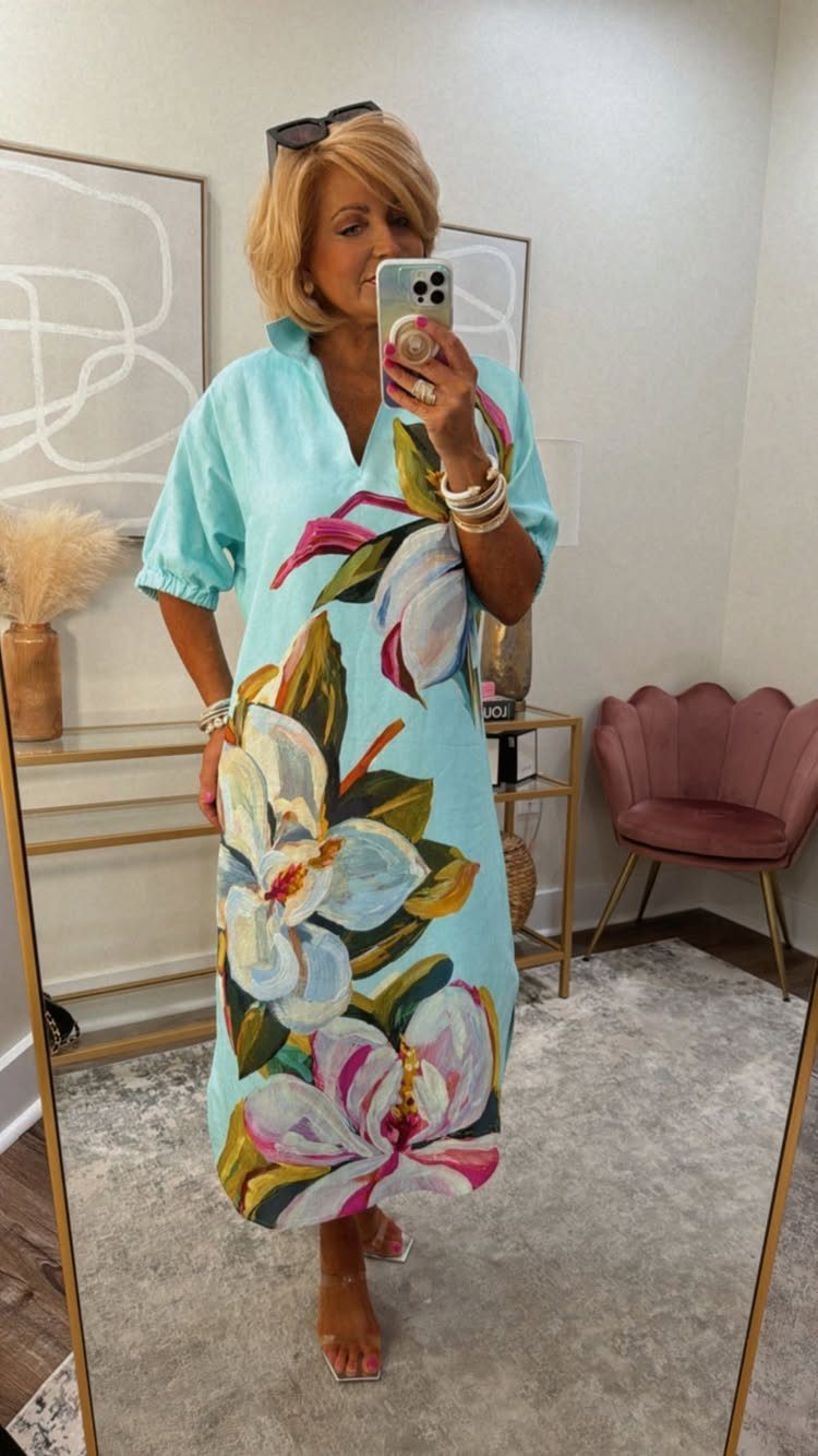 Woman in a light blue floral midi dress taking a mirror selfie.