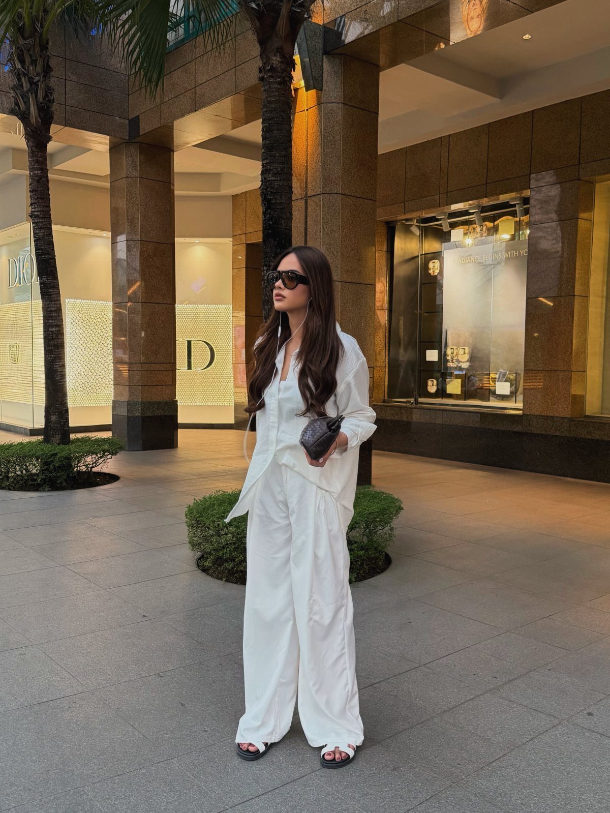Woman in an all-white button-down shirt and wide-leg trousers standing outdoors.