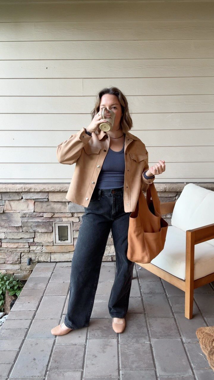 A woman in a tan jacket and black trousers wearing beige pointed-toe flats.