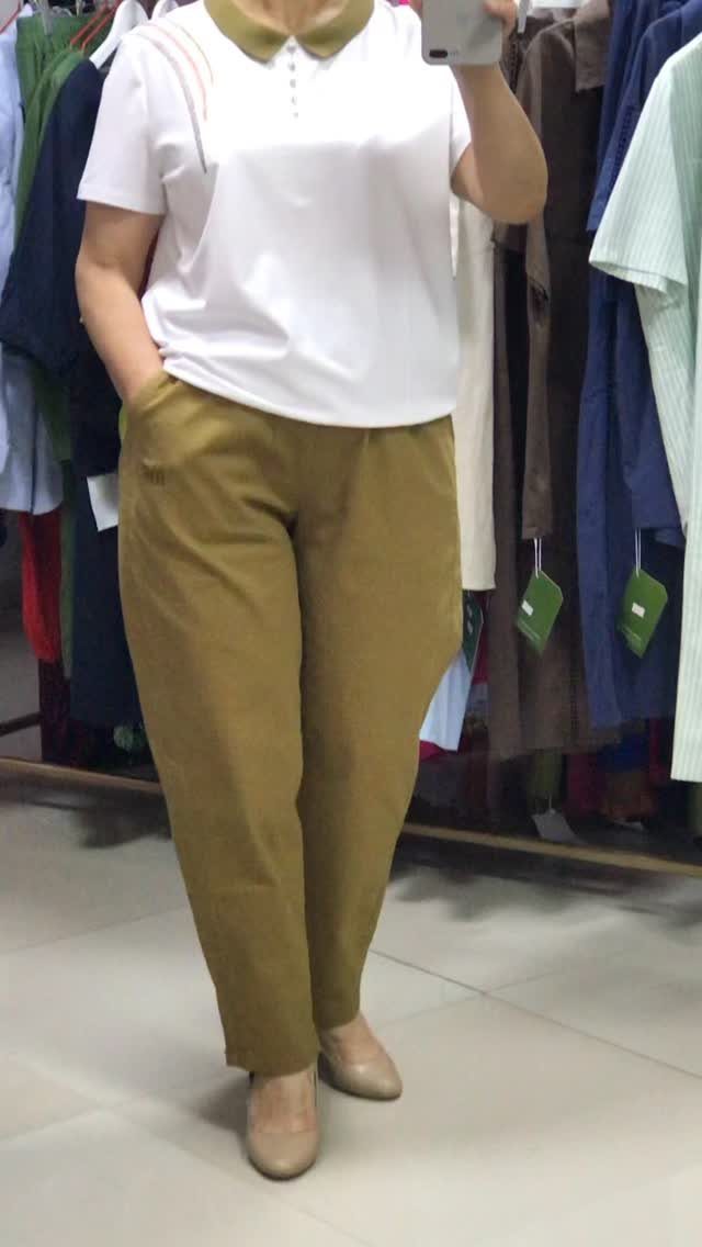 Person wearing a white polo shirt with an olive green collar and olive green trousers.