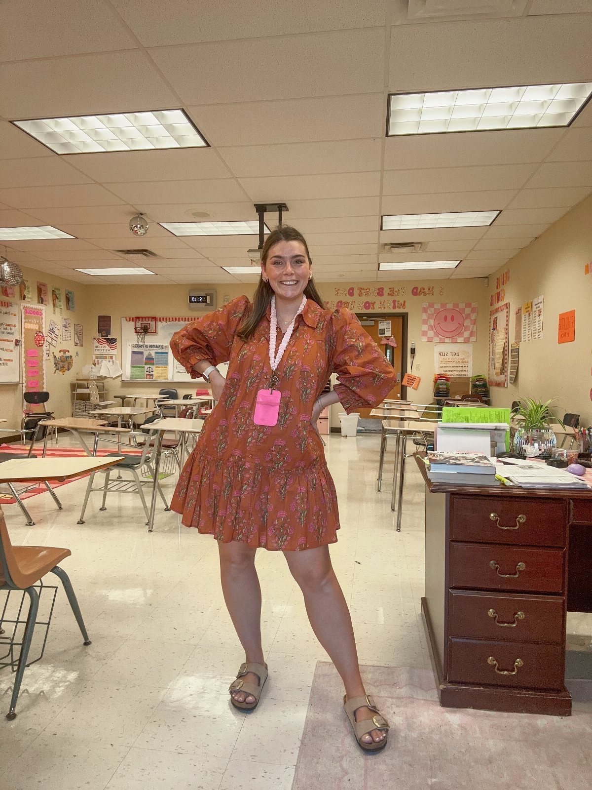Smiling woman in an orange floral puff-sleeve dress standing in a classroom.
