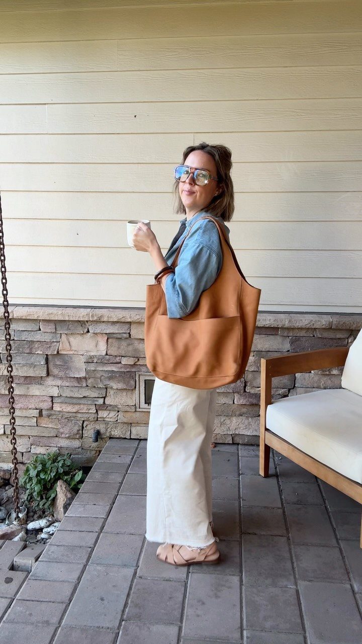 A woman wearing a denim shirt and white wide-leg jeans standing on a patio.