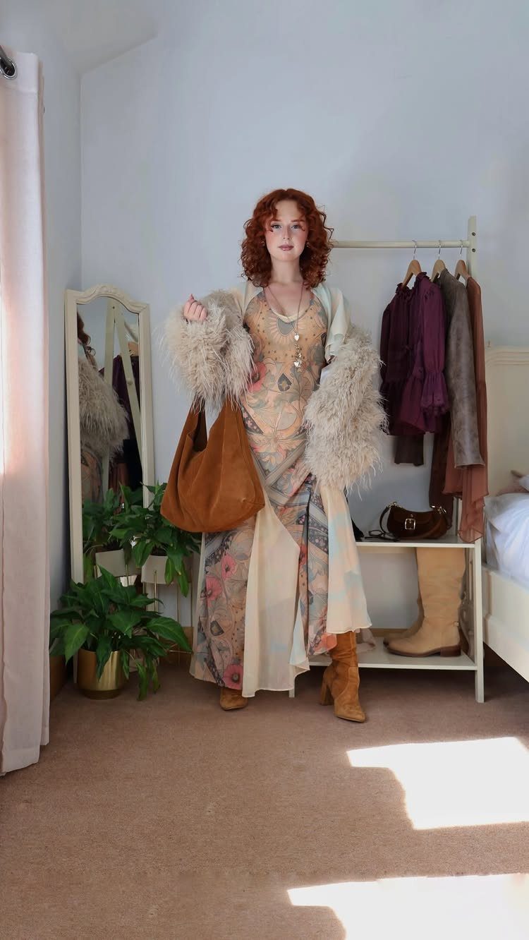 Red-haired woman posing in a long floral dress, fuzzy coat, and brown boots.