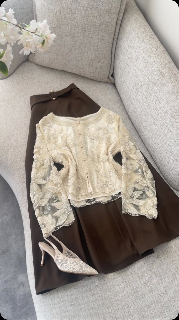 White lace floral top and brown satin skirt with white high heels on a sofa.