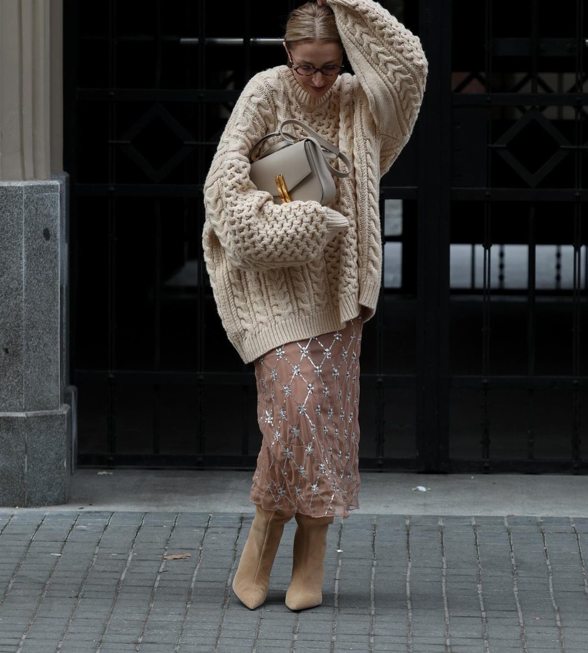 Woman wearing a chunky cream cable-knit oversized sweater and a patterned satin skirt.