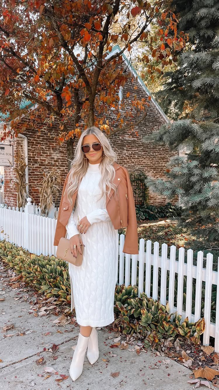 Blonde woman in a white cable-knit sweater dress and tan jacket standing outdoors.