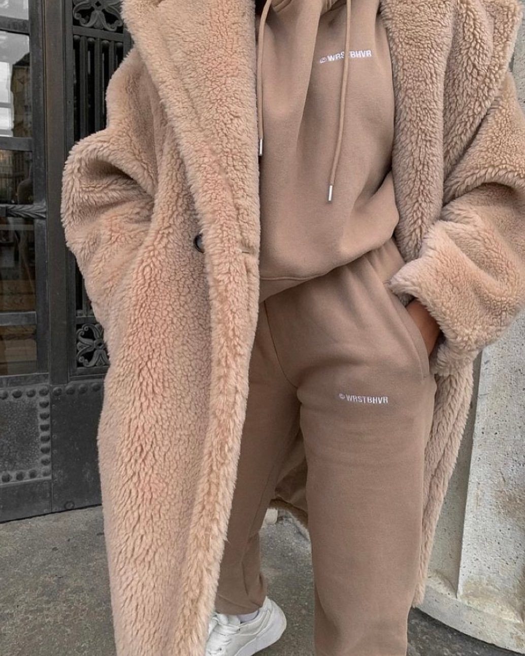 A person wearing a long, tan fuzzy teddy coat over a matching tan sweatsuit.