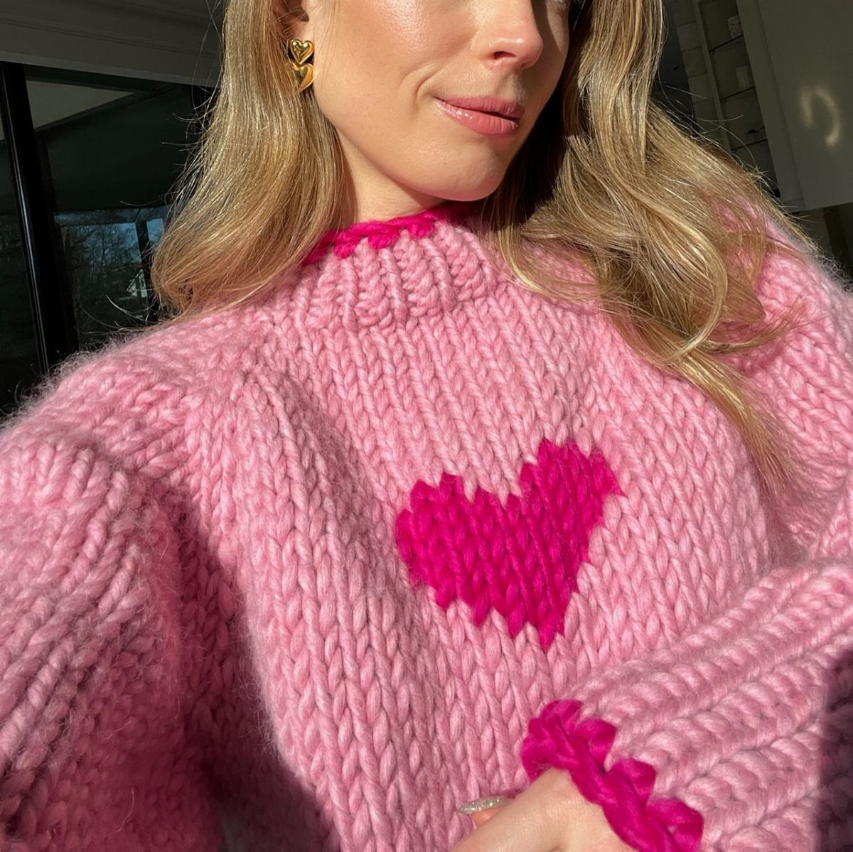 Woman wearing a chunky pink knit sweater with a large bright pink heart design.