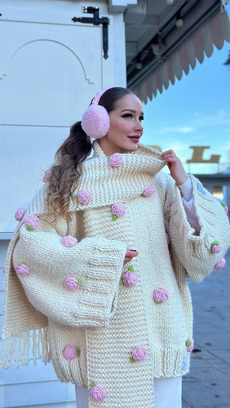 Woman in a cream knit sweater with pink rose details and pink earmuffs.