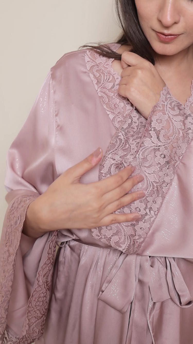 A person wearing a shimmering dusty pink satin robe with delicate lace detailing.