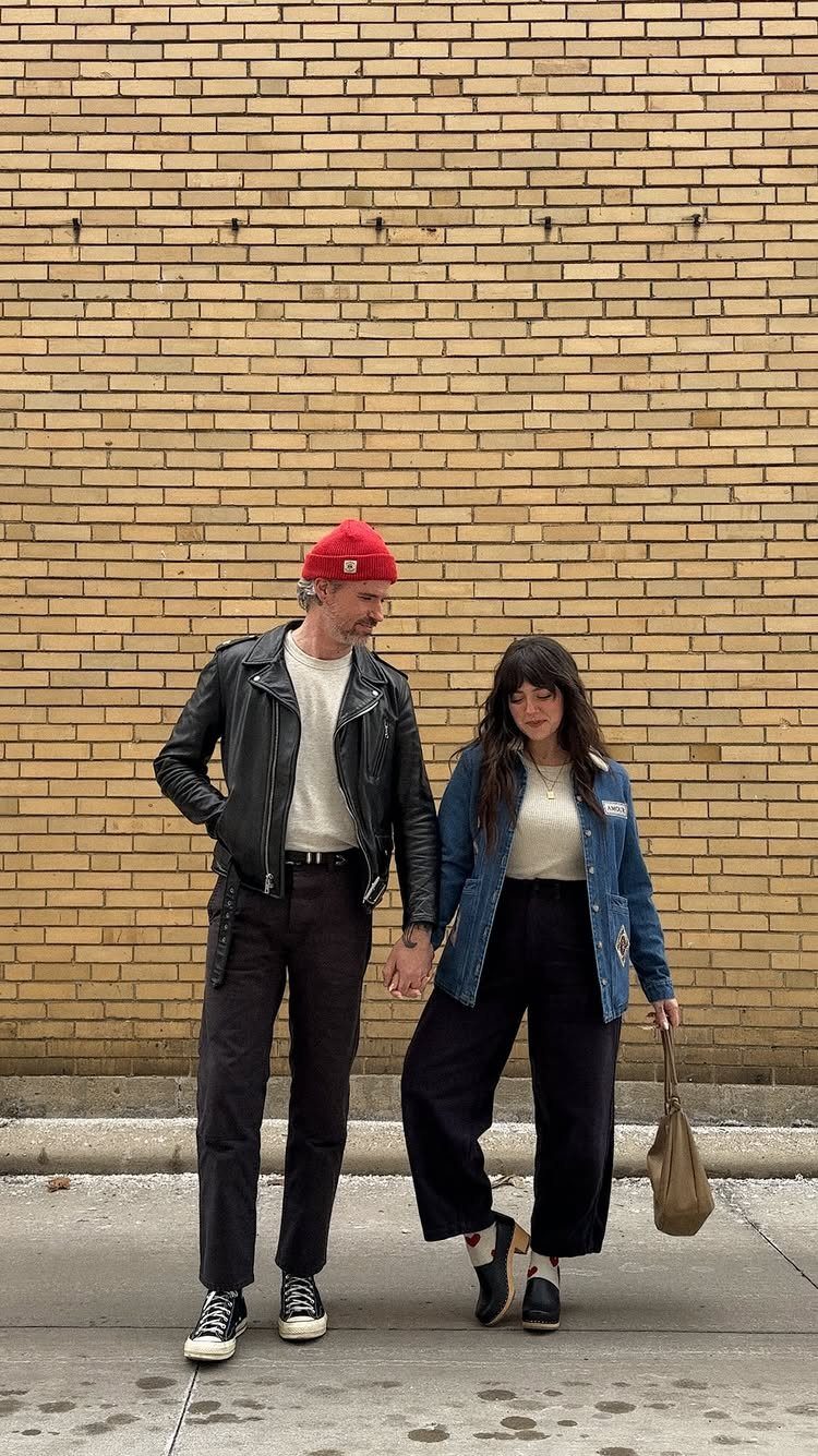 A man in a leather jacket and a woman in a denim jacket walking hand-in-hand.