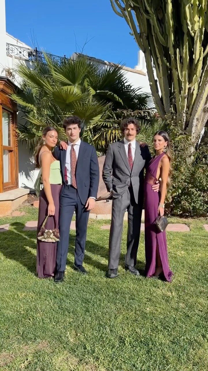 Four young adults in formal attire posing together on a green lawn in a garden.