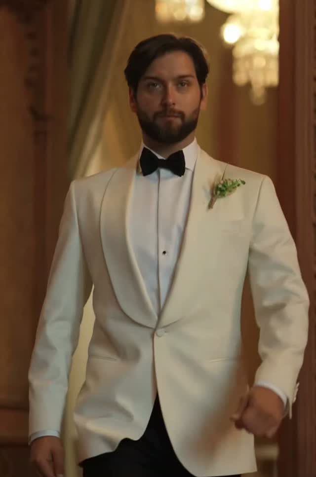 A man wearing a white tuxedo jacket with a black bow tie and boutonniere.