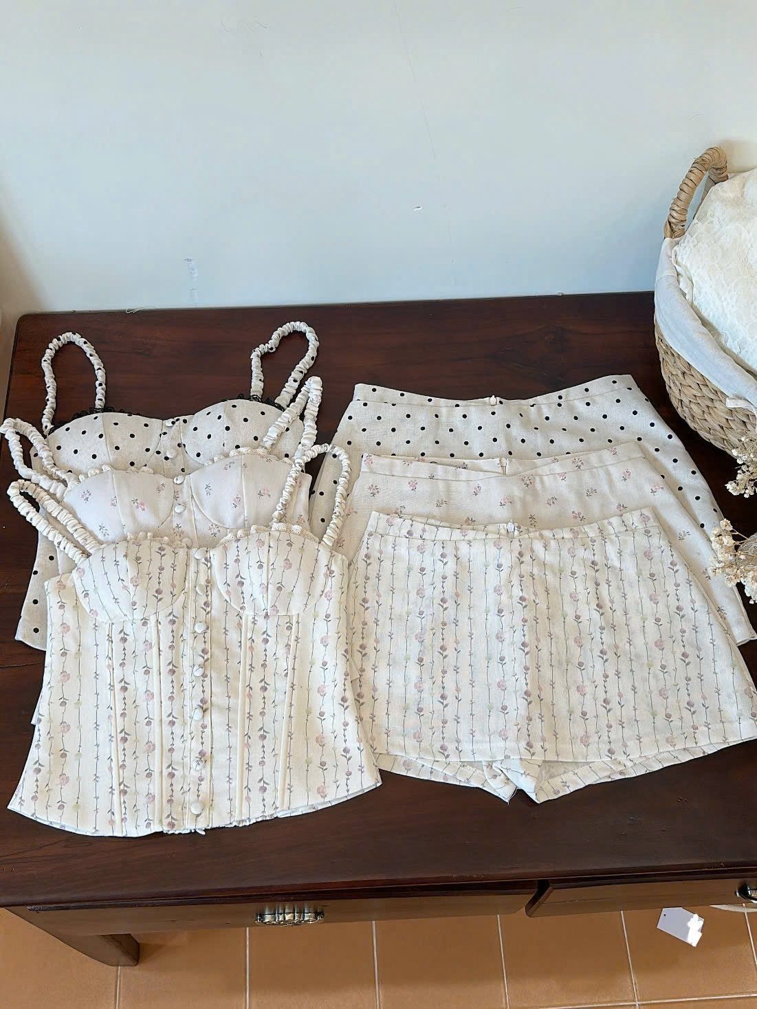 Two sets of cream-colored corset tops and matching shorts laid out on a dark wooden dresser.