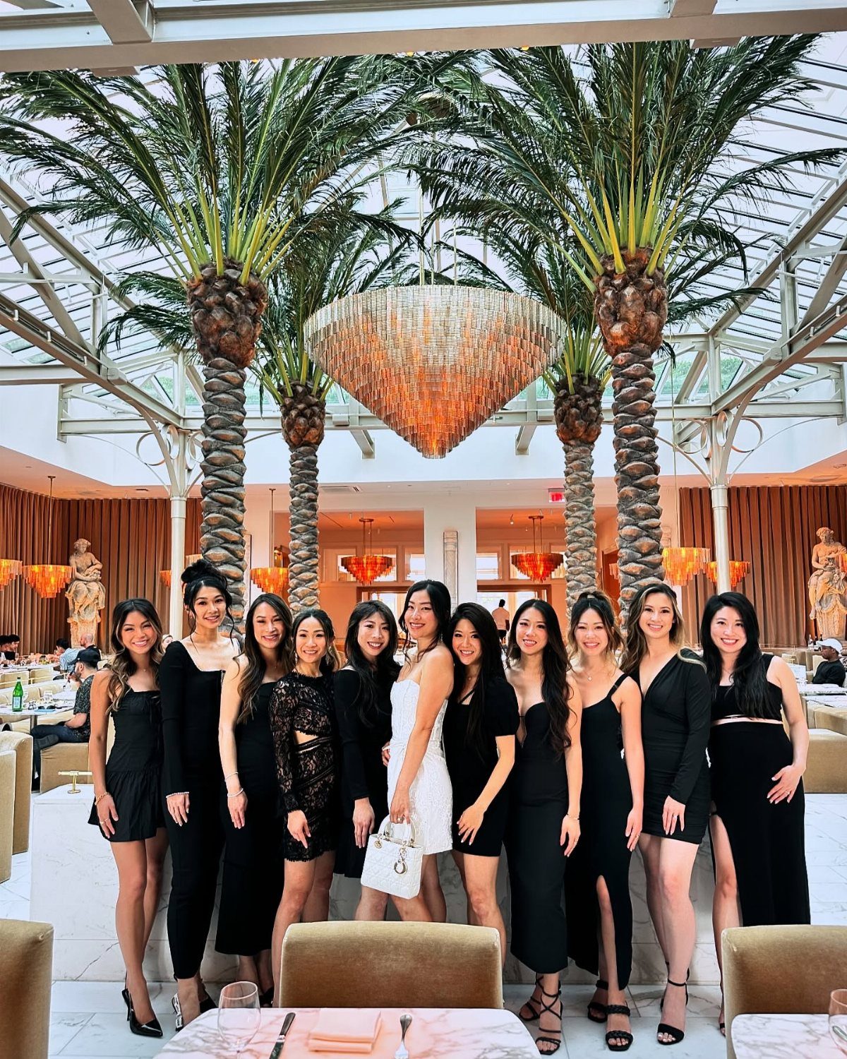 Twelve women posing together in an upscale venue, most wearing black dresses.