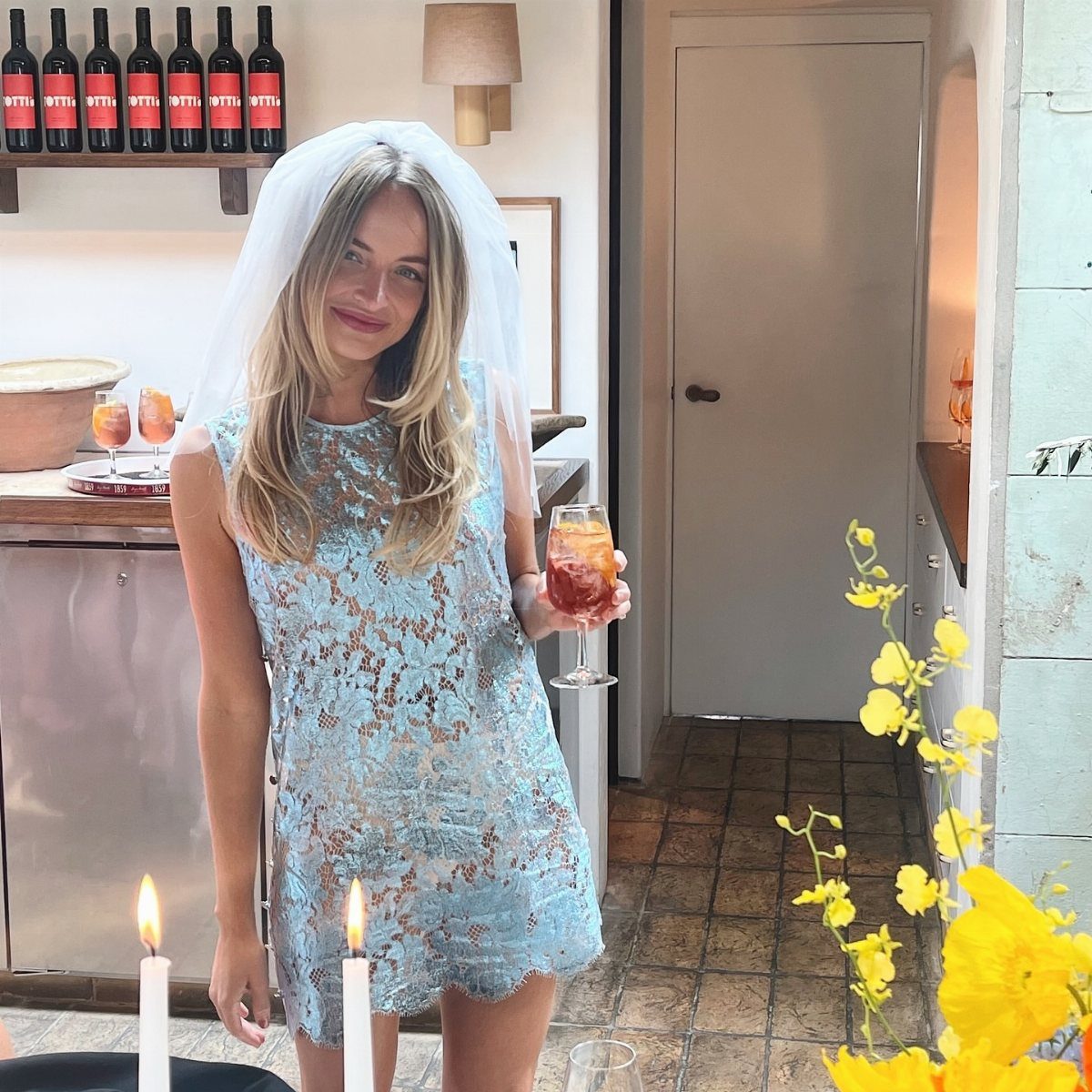 A woman in a blue lace dress and white veil holding a cocktail glass.