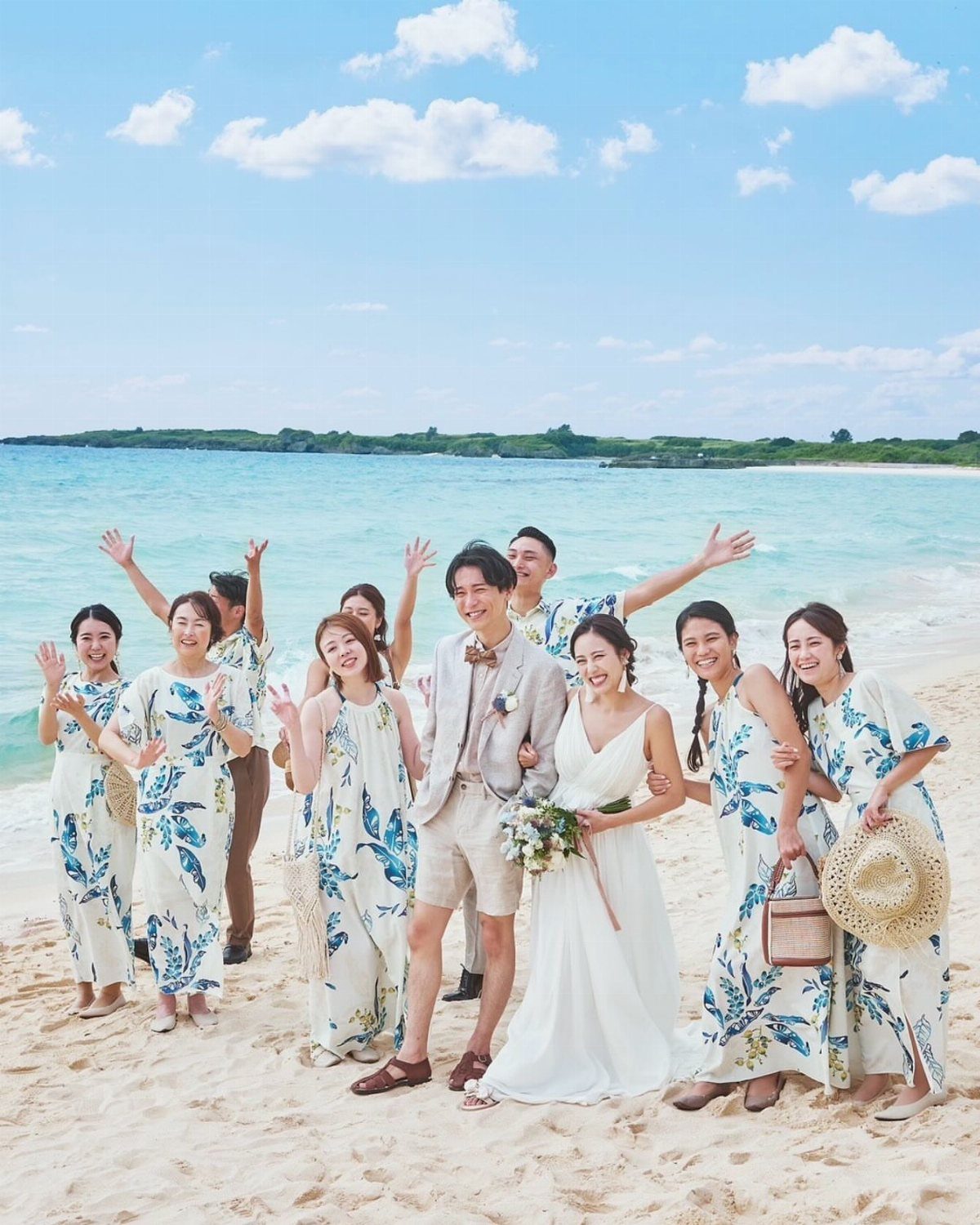 A group of people in tropical print dresses and wedding attire posing on a sunny beach.