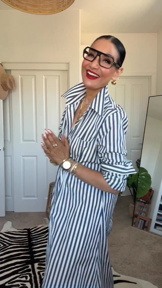 Smiling woman wearing a blue and white striped shirtdress and large black glasses.