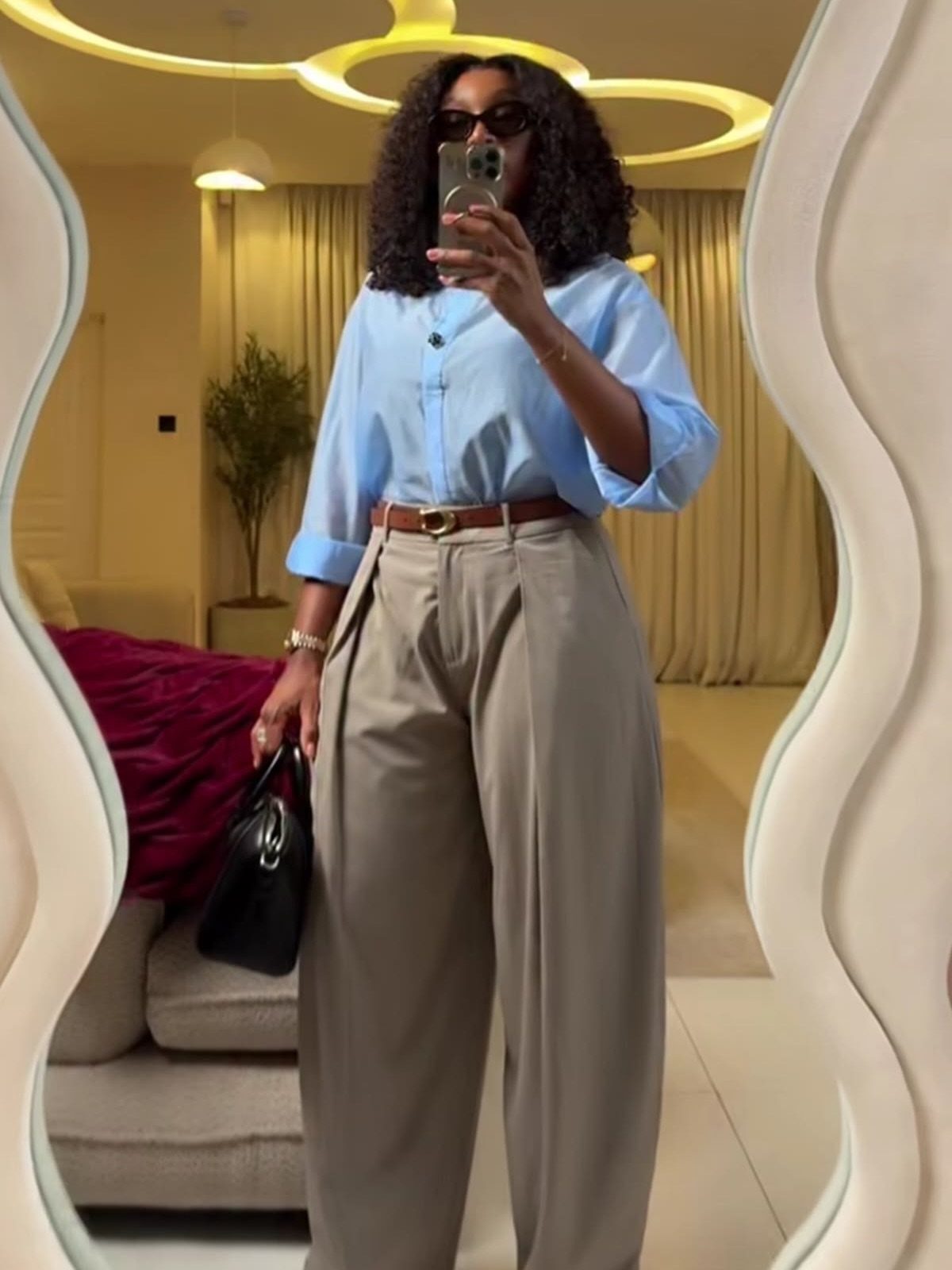 Woman posing in a mirror wearing a blue button-up shirt and beige wide-leg trousers.