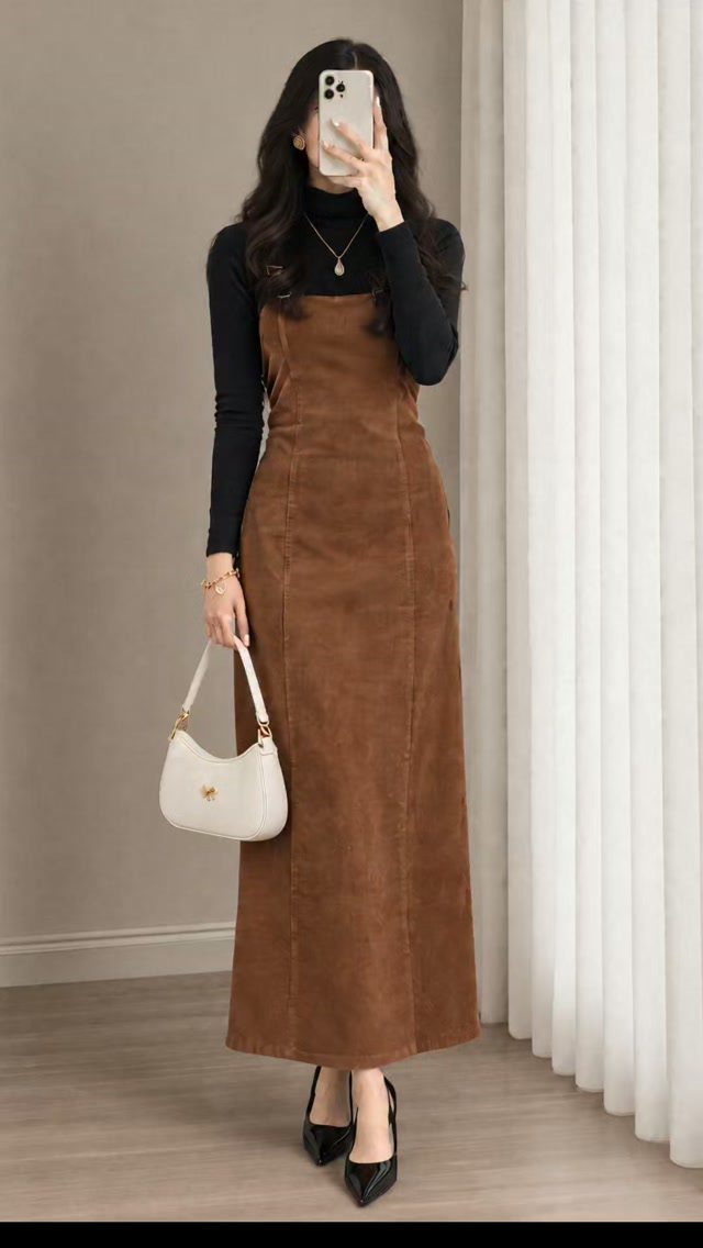 Woman in a black turtleneck and brown corduroy maxi dress holding a white handbag.