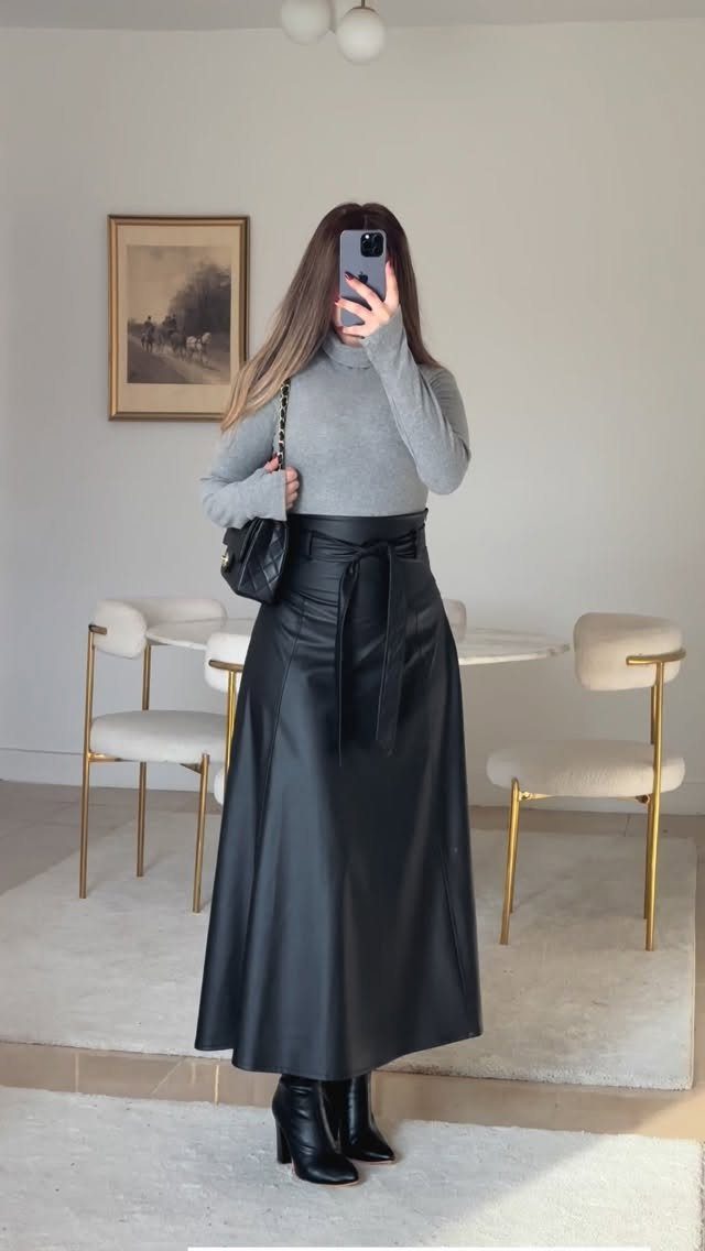Person wearing a grey turtleneck, black leather midi skirt, and black ankle boots.