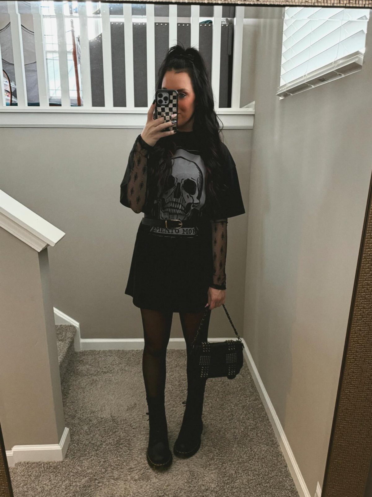 Woman posing in a black skull t-shirt, mini skirt, tights, and boots for a concert outfit.
