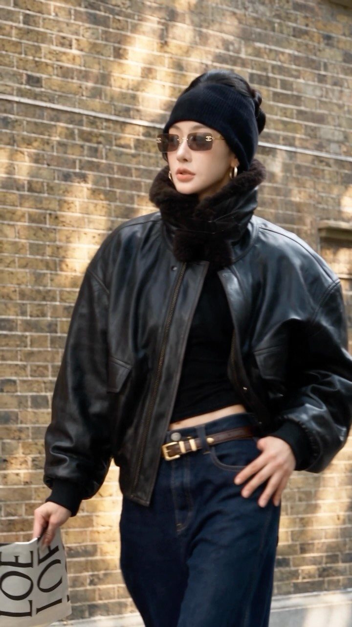 Woman in a black leather bomber jacket, black beanie, and dark blue denim jeans.