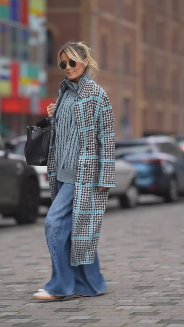 Woman walking in a blue plaid coat, blue knit sweater, and wide-leg denim jeans.