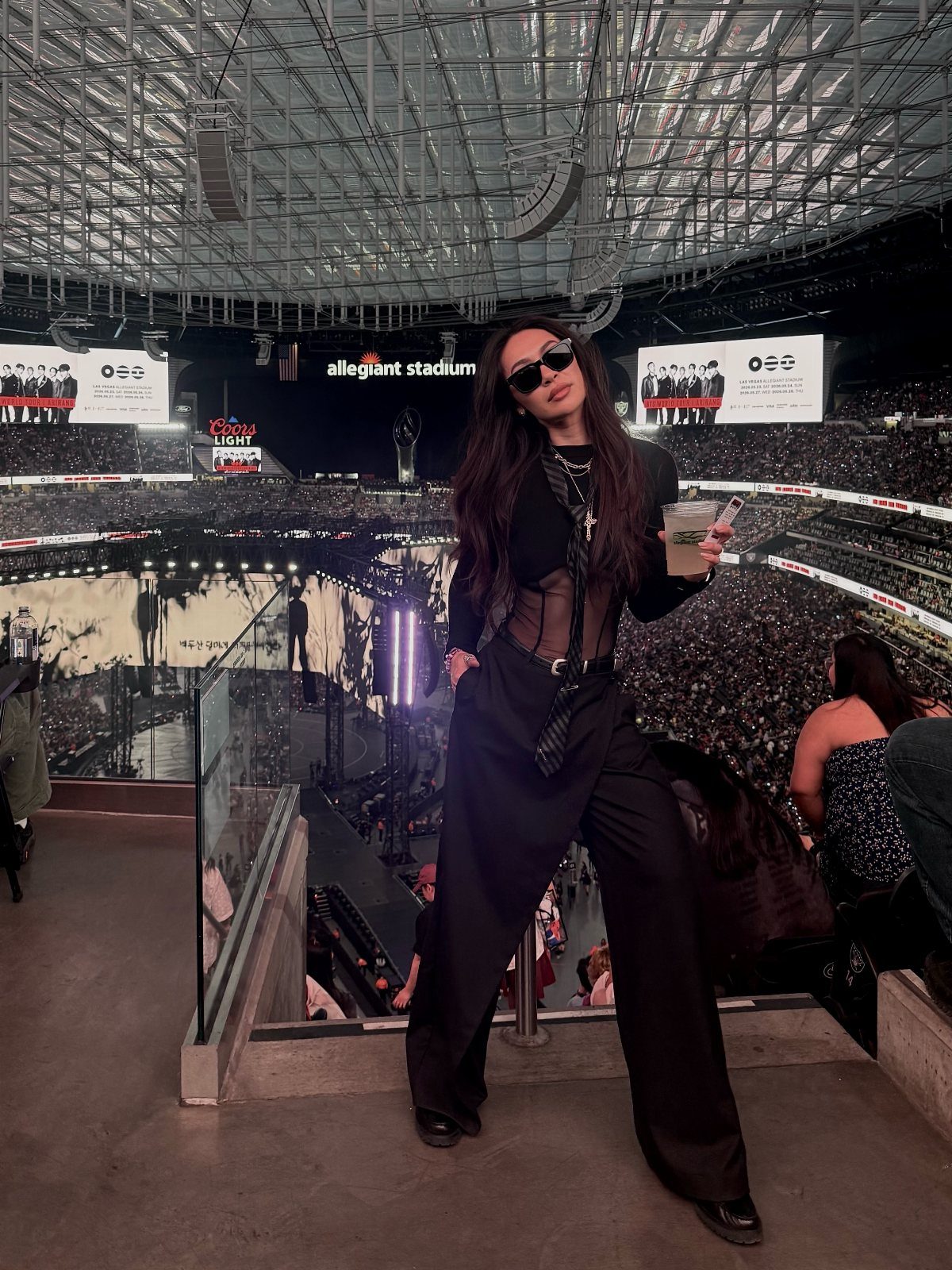Woman in black outfit posing in a large, crowded stadium at night.