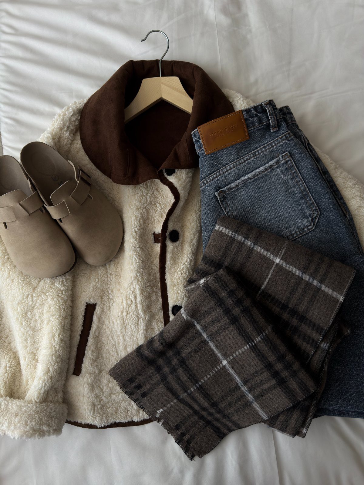 Cream teddy coat with brown collar, corduroy jeans, tan clogs, and a plaid scarf.