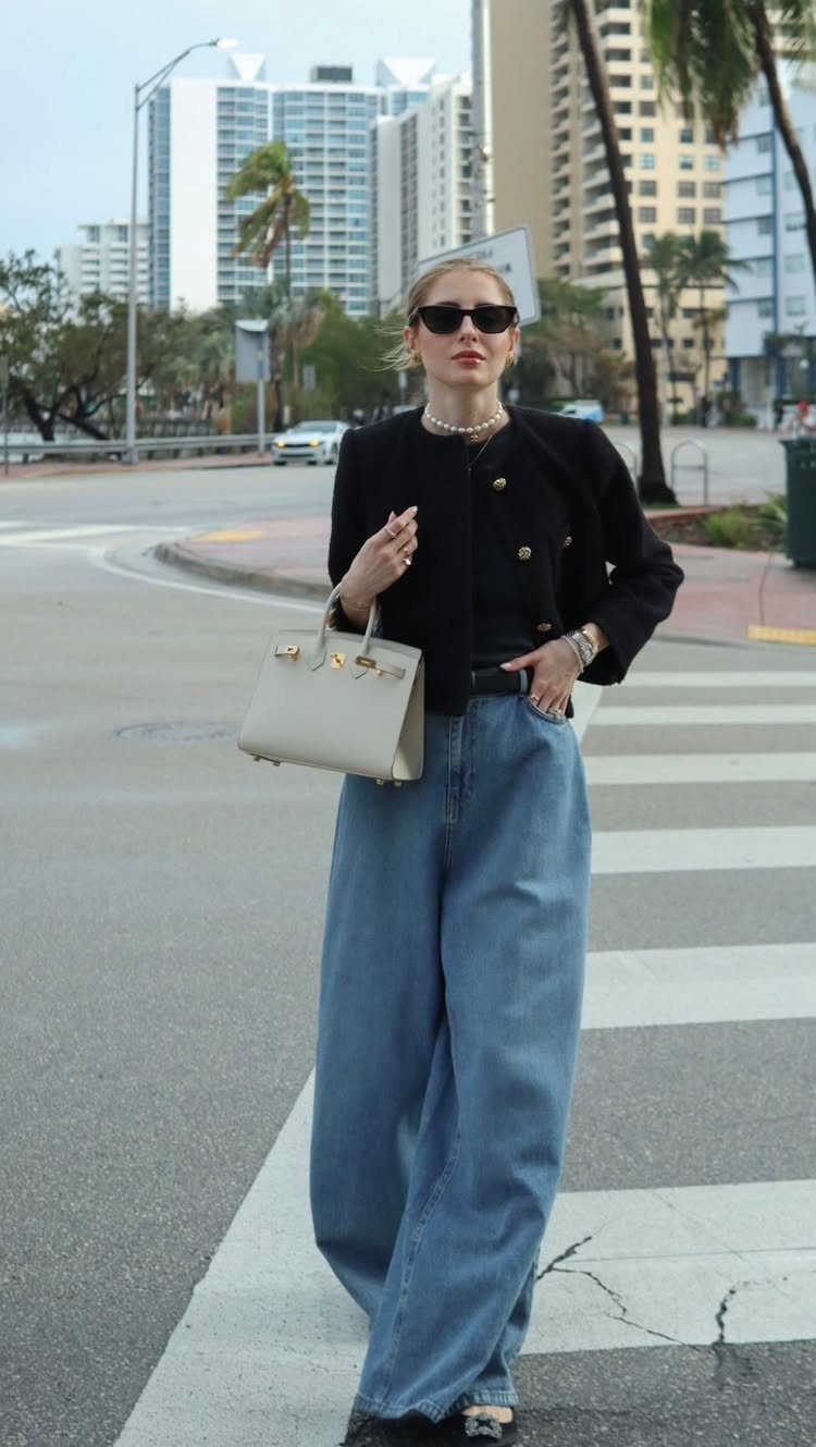 Woman wearing a black jacket and light blue wide-leg denim jeans on a city street.