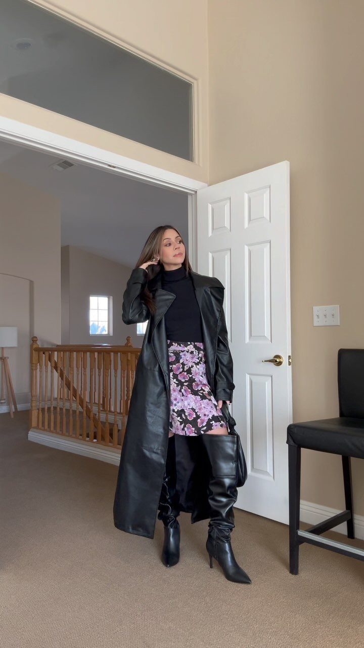 Woman wearing a long black leather coat, floral skirt, and black thigh-high boots.