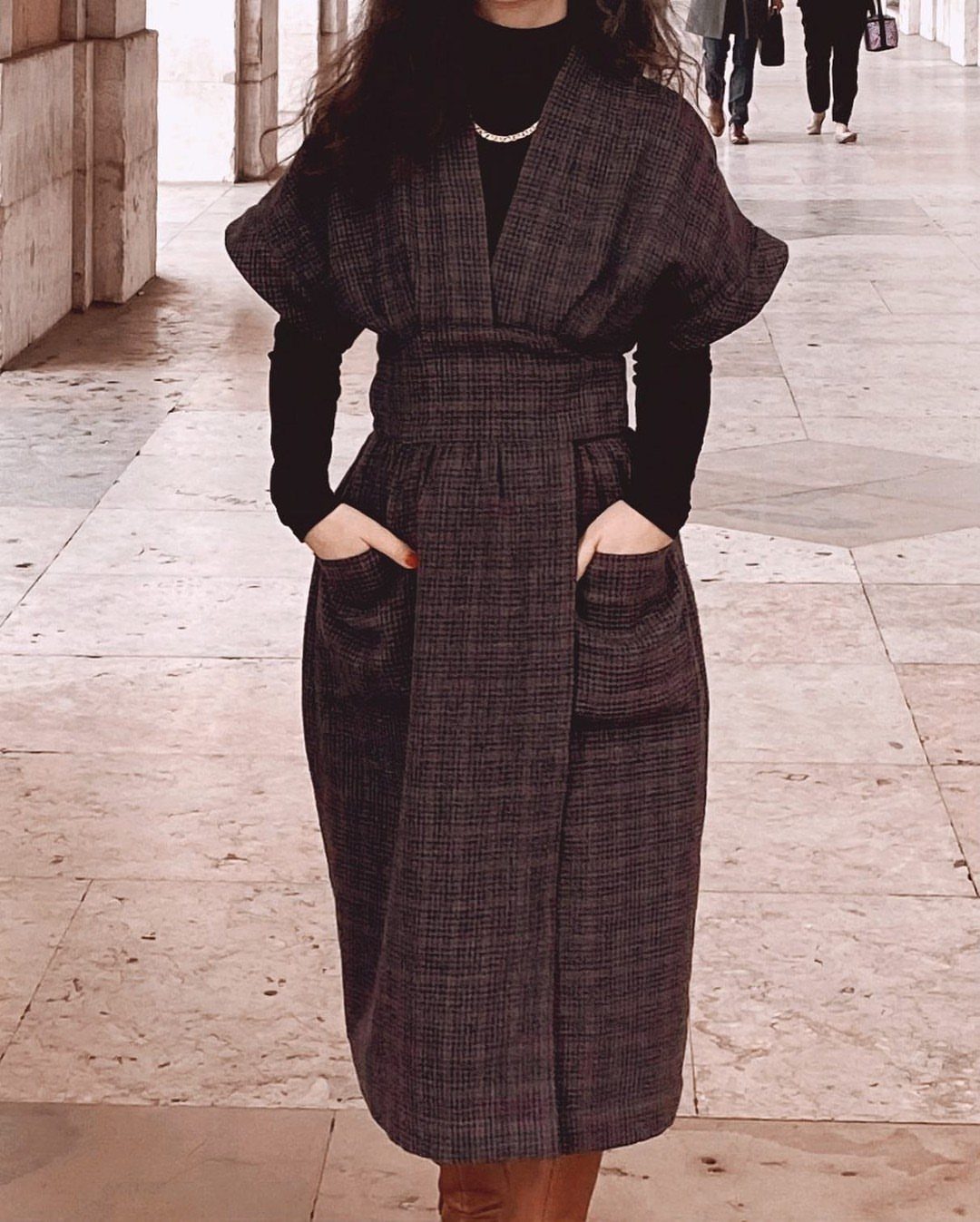 A person wearing a dark patterned wrap dress with voluminous sleeves over a black turtleneck.