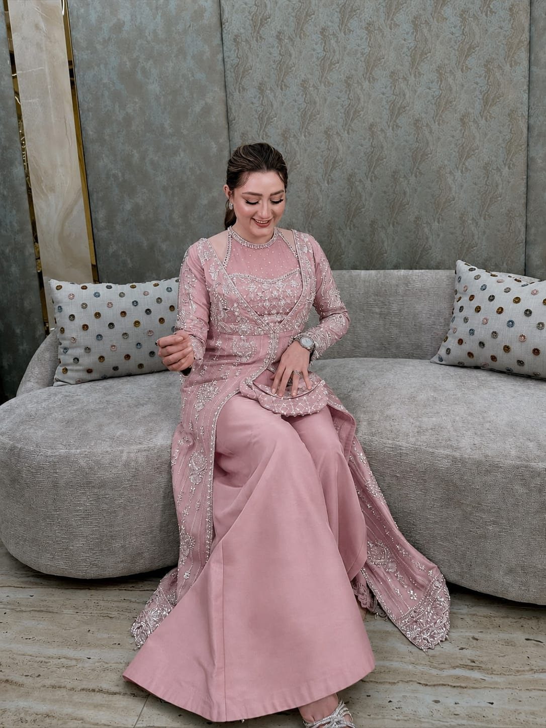 Woman in a dusty pink embellished long-sleeved tunic and matching maxi skirt sitting on a sofa.
