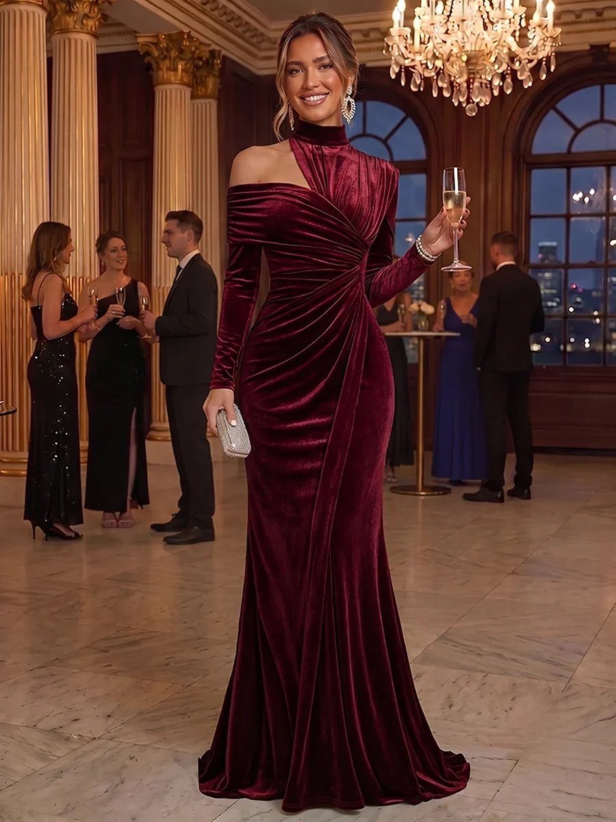 A woman in a long-sleeved burgundy velvet dress poses in a grand ballroom holding champagne.