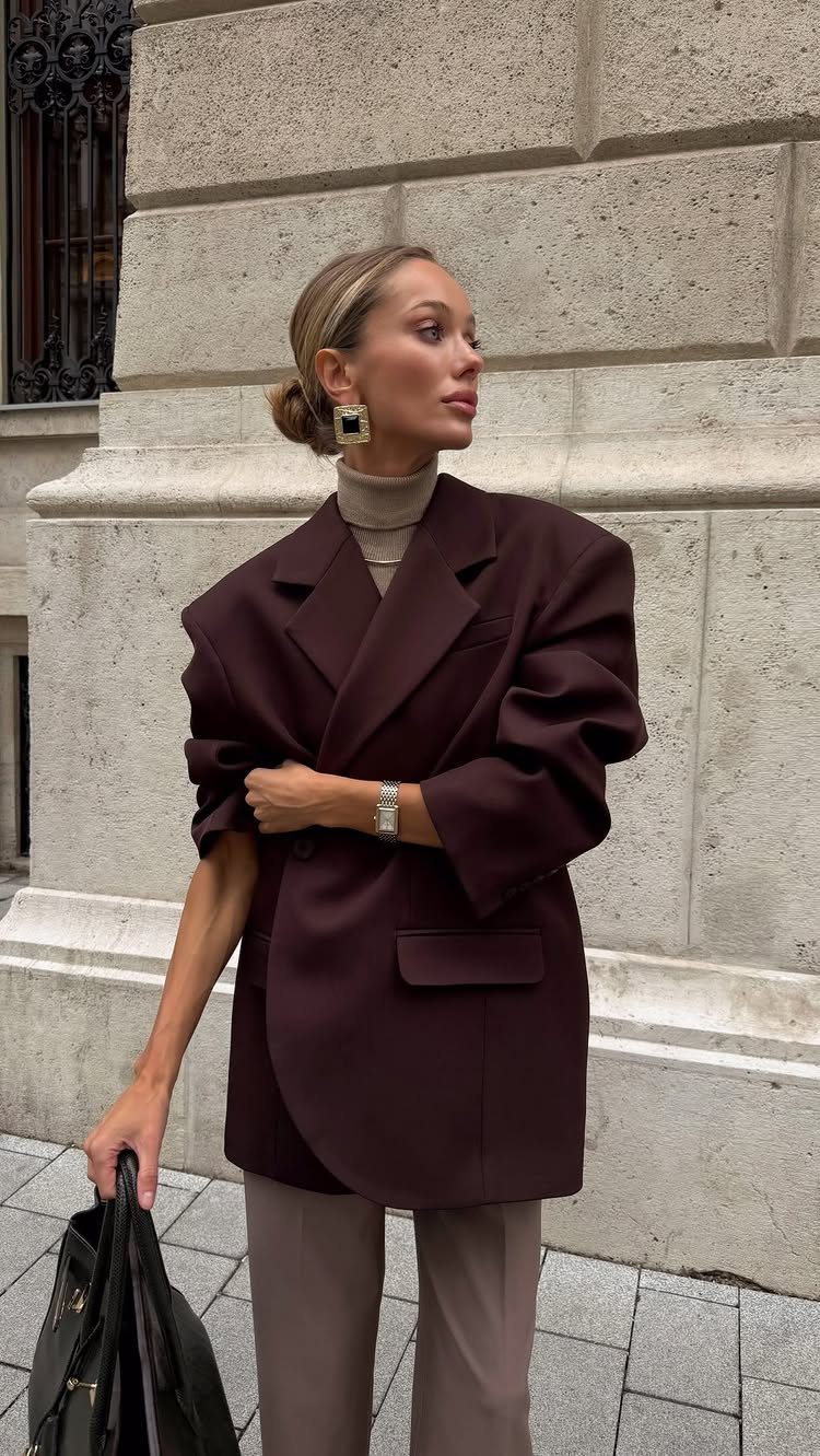 Woman wearing a dark burgundy oversized blazer, beige turtleneck, and taupe trousers outdoors.