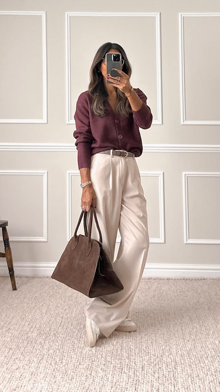 Woman in maroon cardigan and cream wide-leg trousers holding a brown suede tote bag.