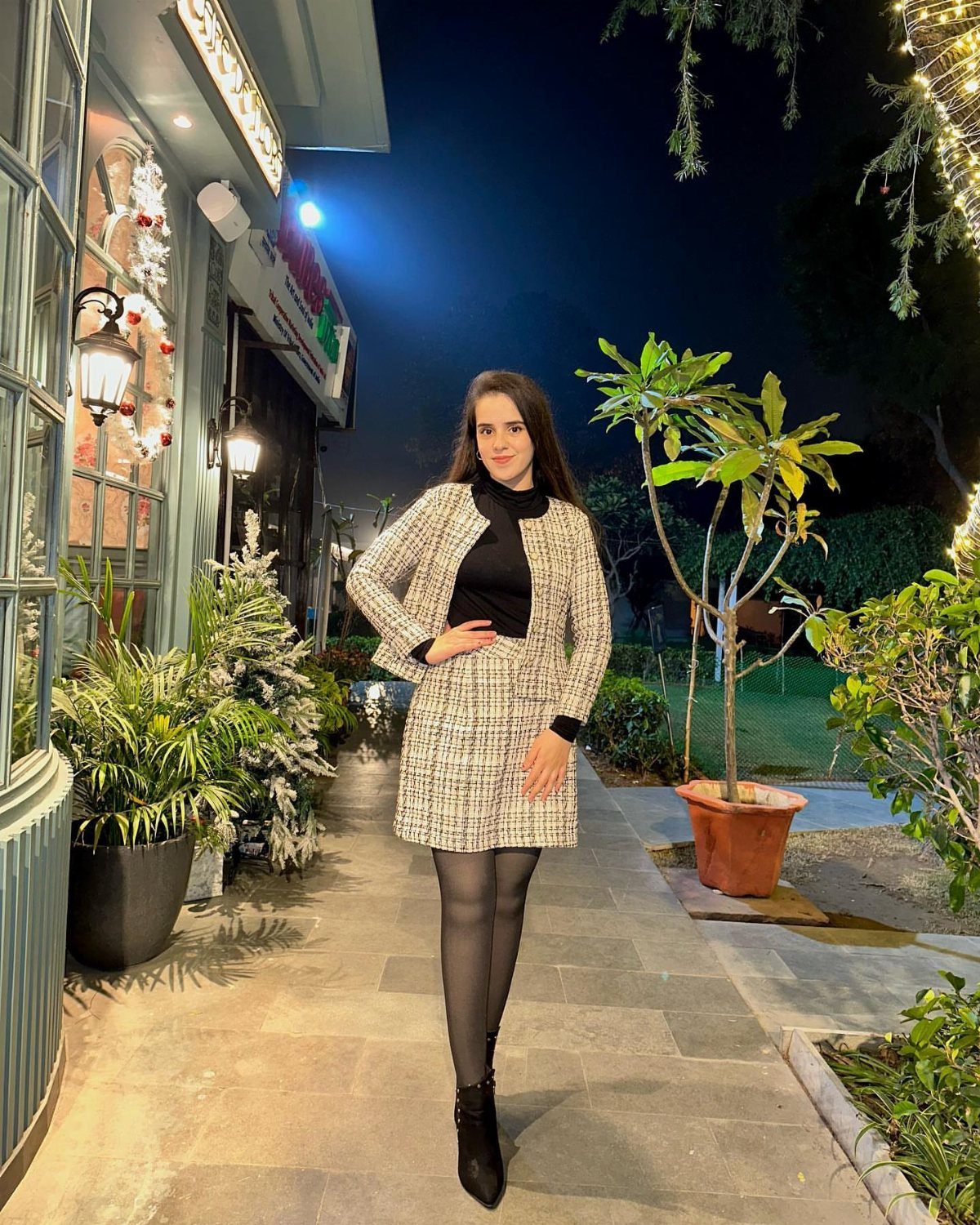 Woman in a white and black patterned tweed skirt suit and black tights standing outdoors at night.