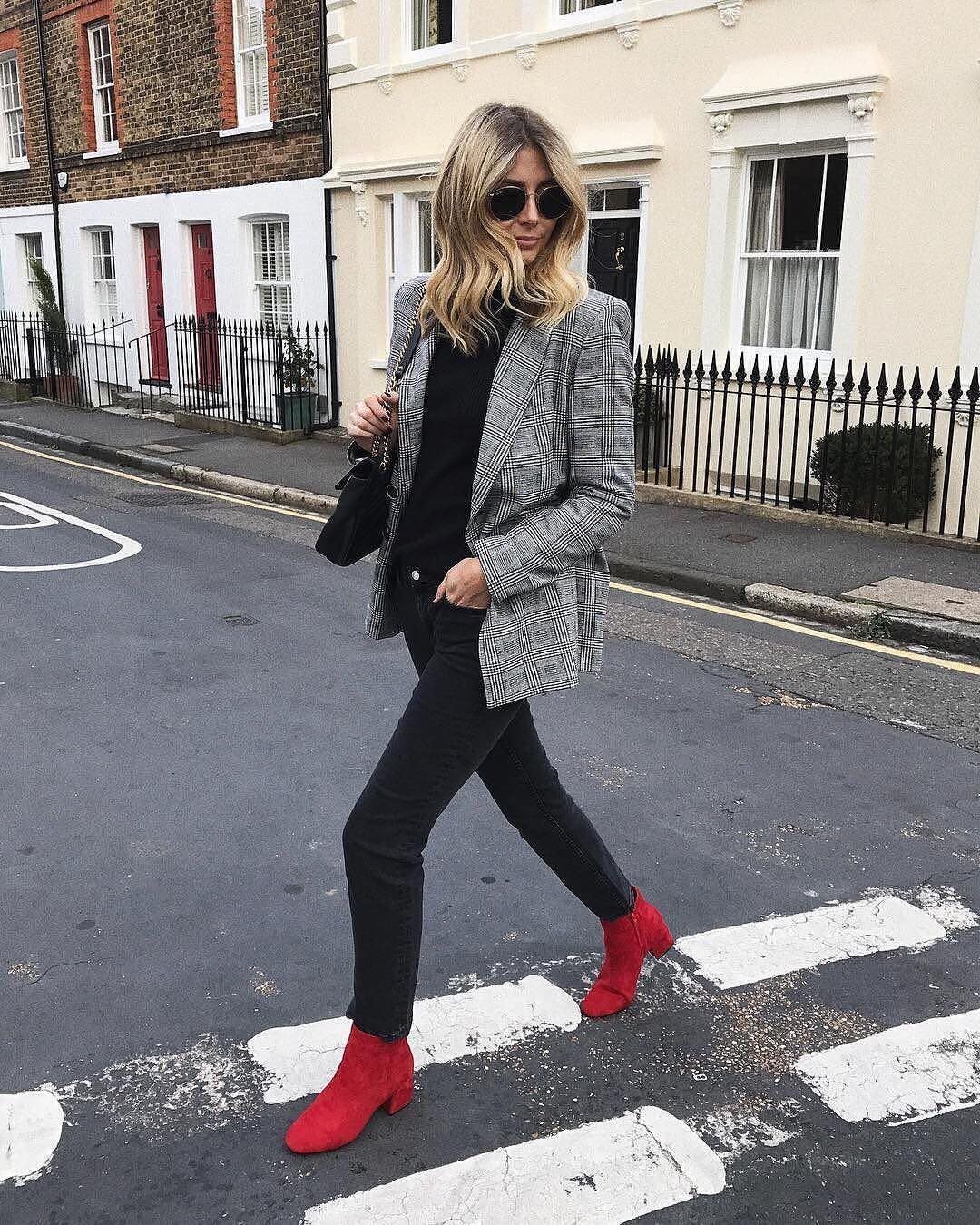 Woman in a plaid blazer, black pants, and bright red ankle boots walking across a street.
