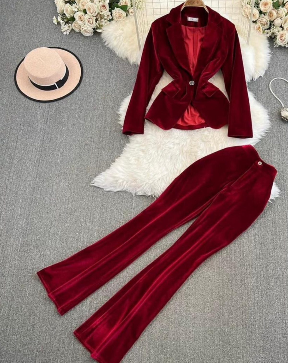 Red velvet blazer and matching flared pants laid on white faux fur with a hat.