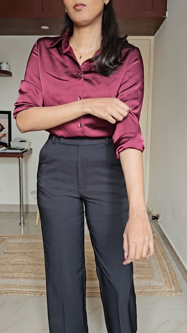 A woman wearing a magenta satin blouse and dark grey tailored trousers standing indoors.