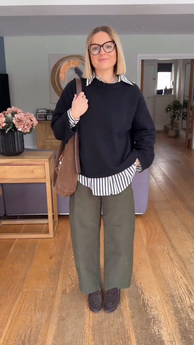 Woman wearing a black sweater, striped shirt, olive wide-leg pants, and dark loafers.