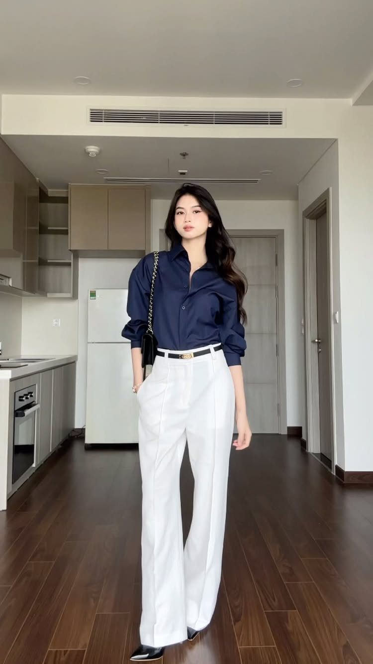 Woman wearing a navy blue button-down shirt and white wide-leg trousers standing in a kitchen.
