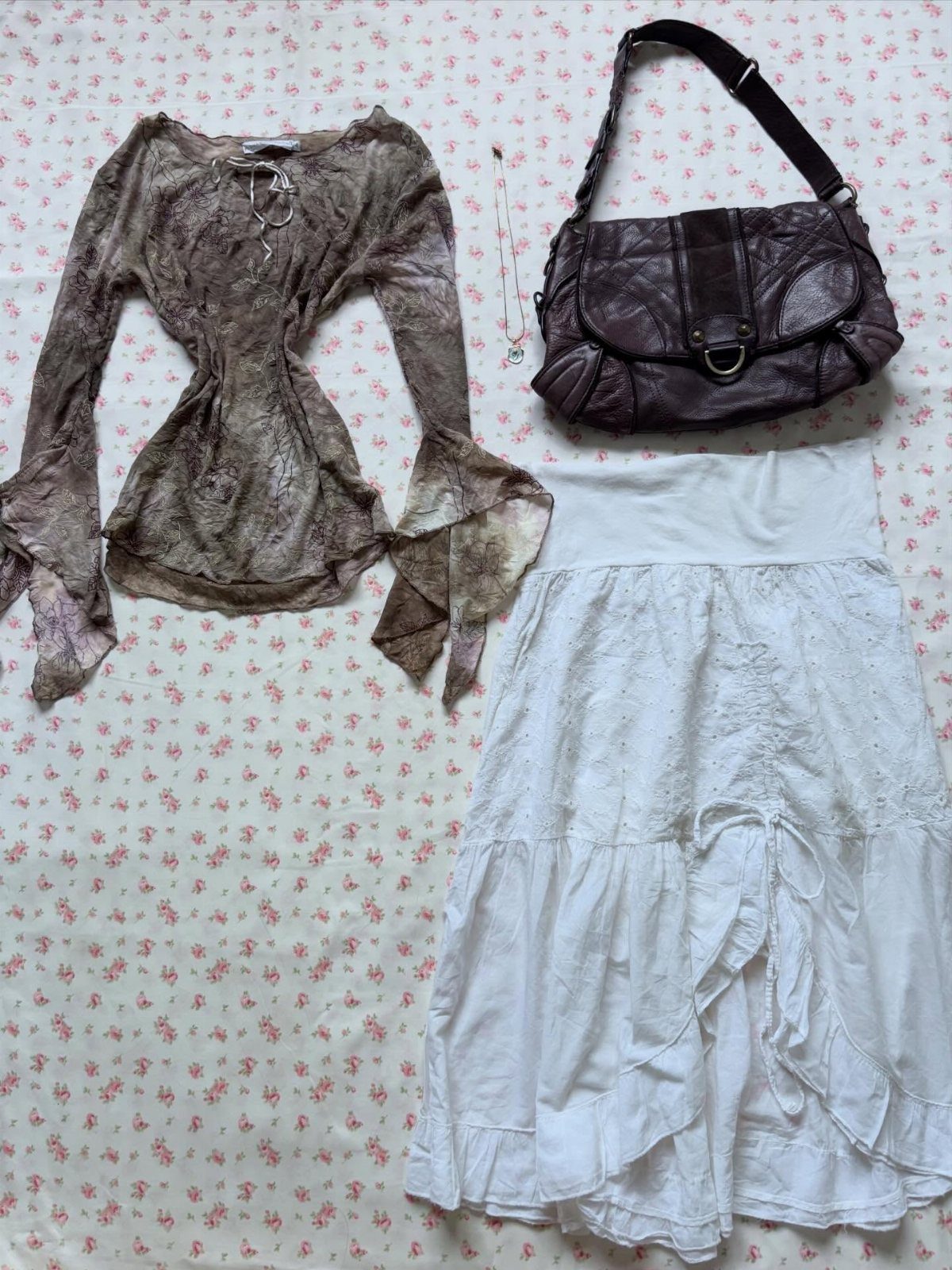 A brown patterned top, white lace skirt, and brown leather bag laid on floral fabric.