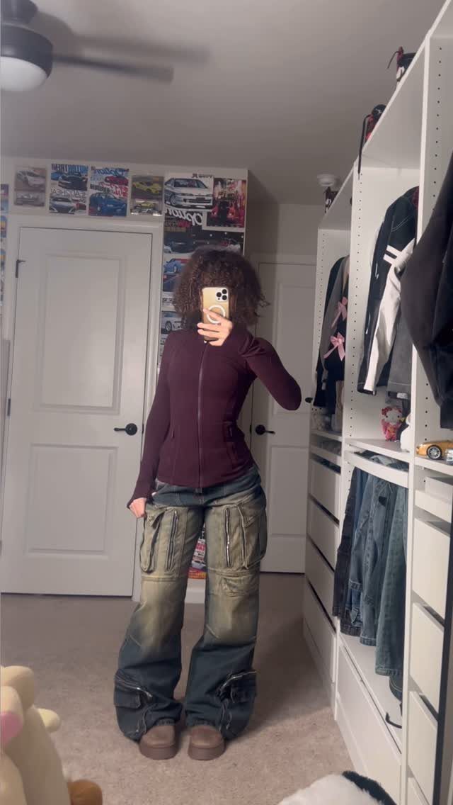 Person wearing a purple zip-up top and baggy denim cargo pants posing in a mirror.