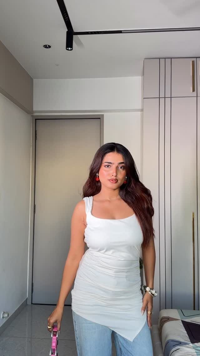 Woman wearing a white ruched top layered over light blue denim jeans.