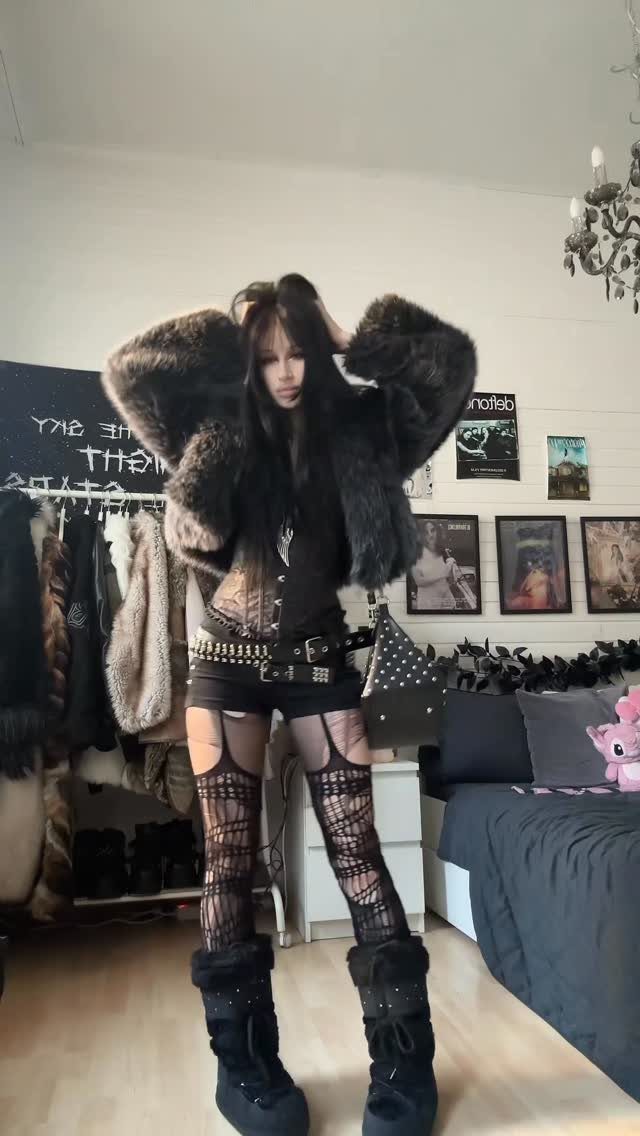 A person posing in a black outfit with a large faux fur coat and patterned tights.
